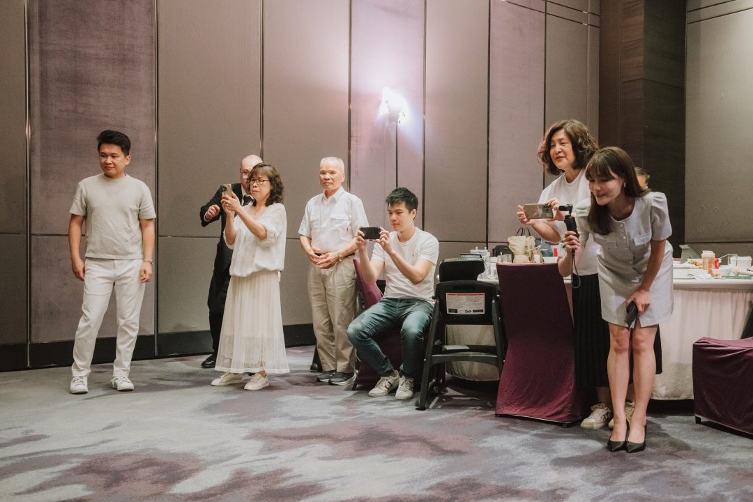 全家親友站在宴會桌旁紛紛拿出手機，專心拍攝孩子互動。