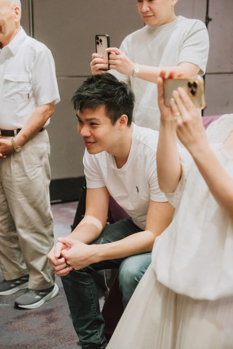 坐在紫椅上的男子溫柔看著孩子，身後家人舉手機拍照。