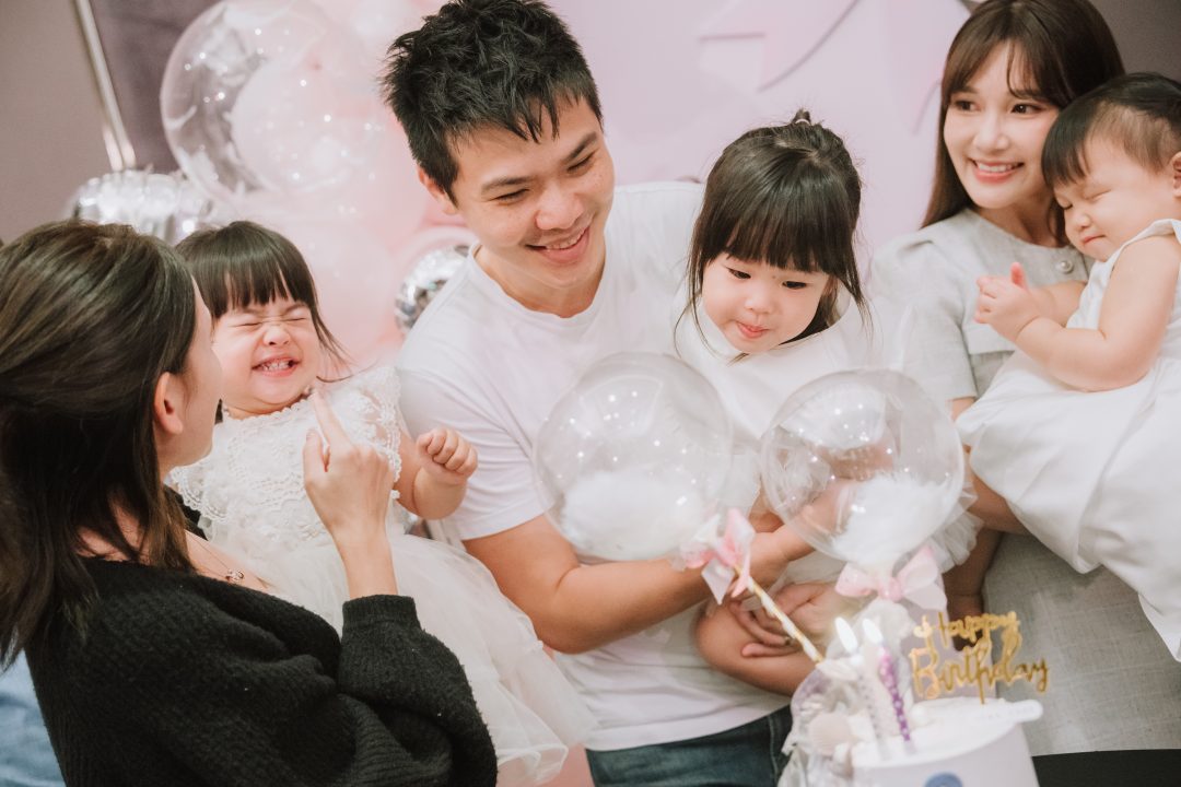 身穿白衣的父親抱著手拿羽毛透明氣球的女兒