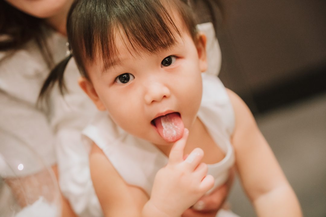 穿白洋裝的小女孩伸出沾著白色奶油的舌頭看向鏡頭