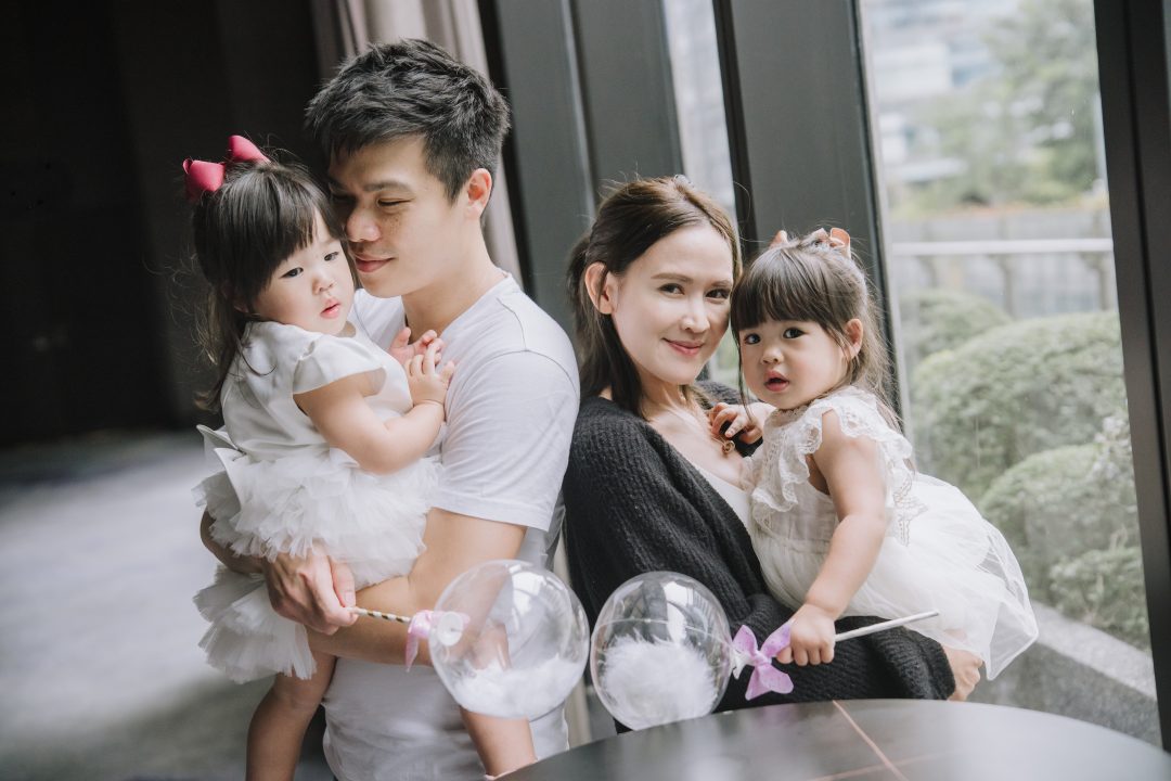 爸爸溫柔注視懷中的女兒，媽媽抱著另一個孩子看鏡頭