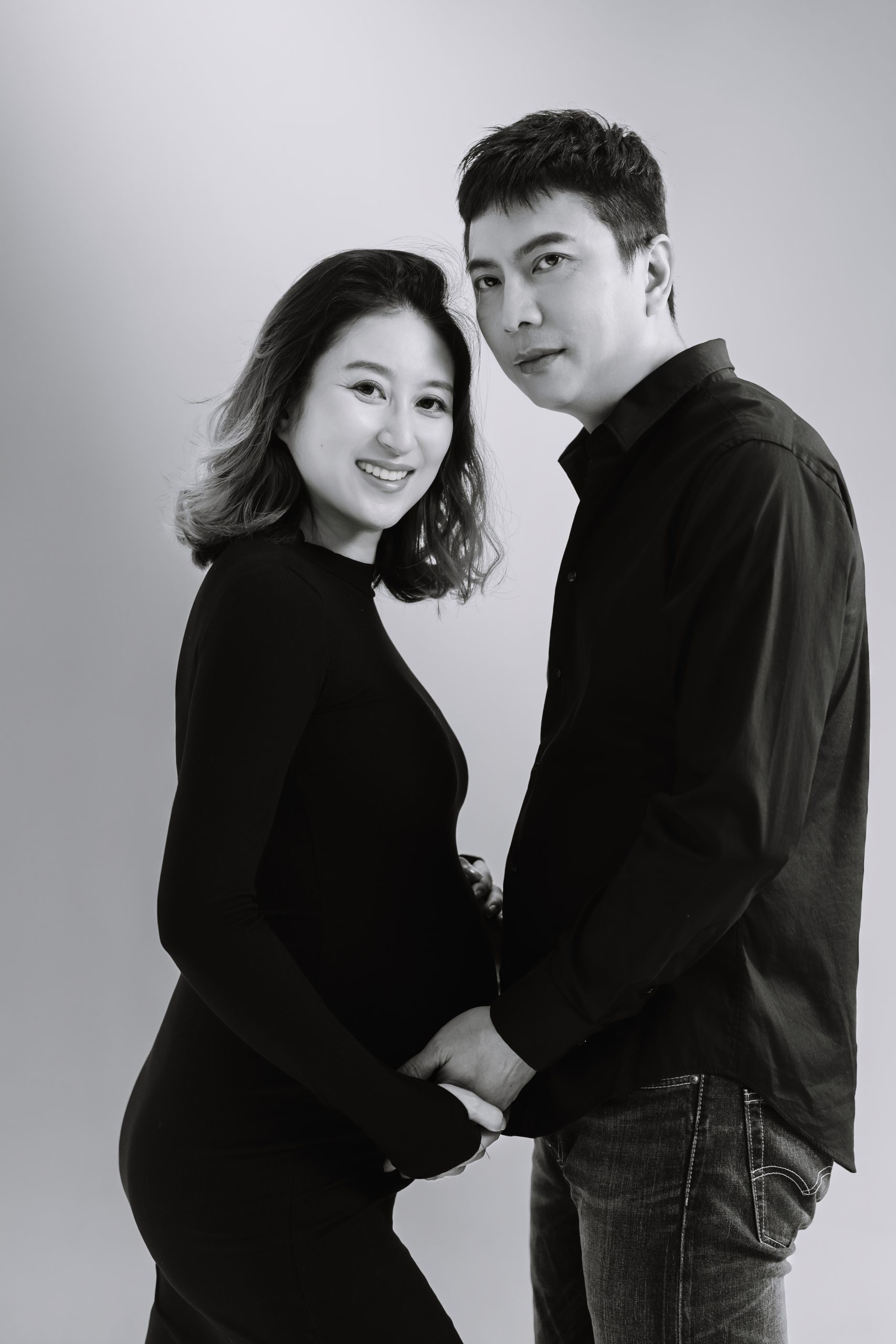 兩人面對鏡頭並肩微笑，先生雙手包覆著太太按在肚上的手掌。