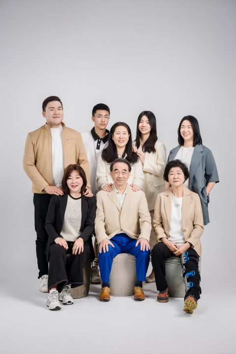 八名家族成員在純白背景棚內合影，長輩坐於圓凳、後排家人搭肩微笑