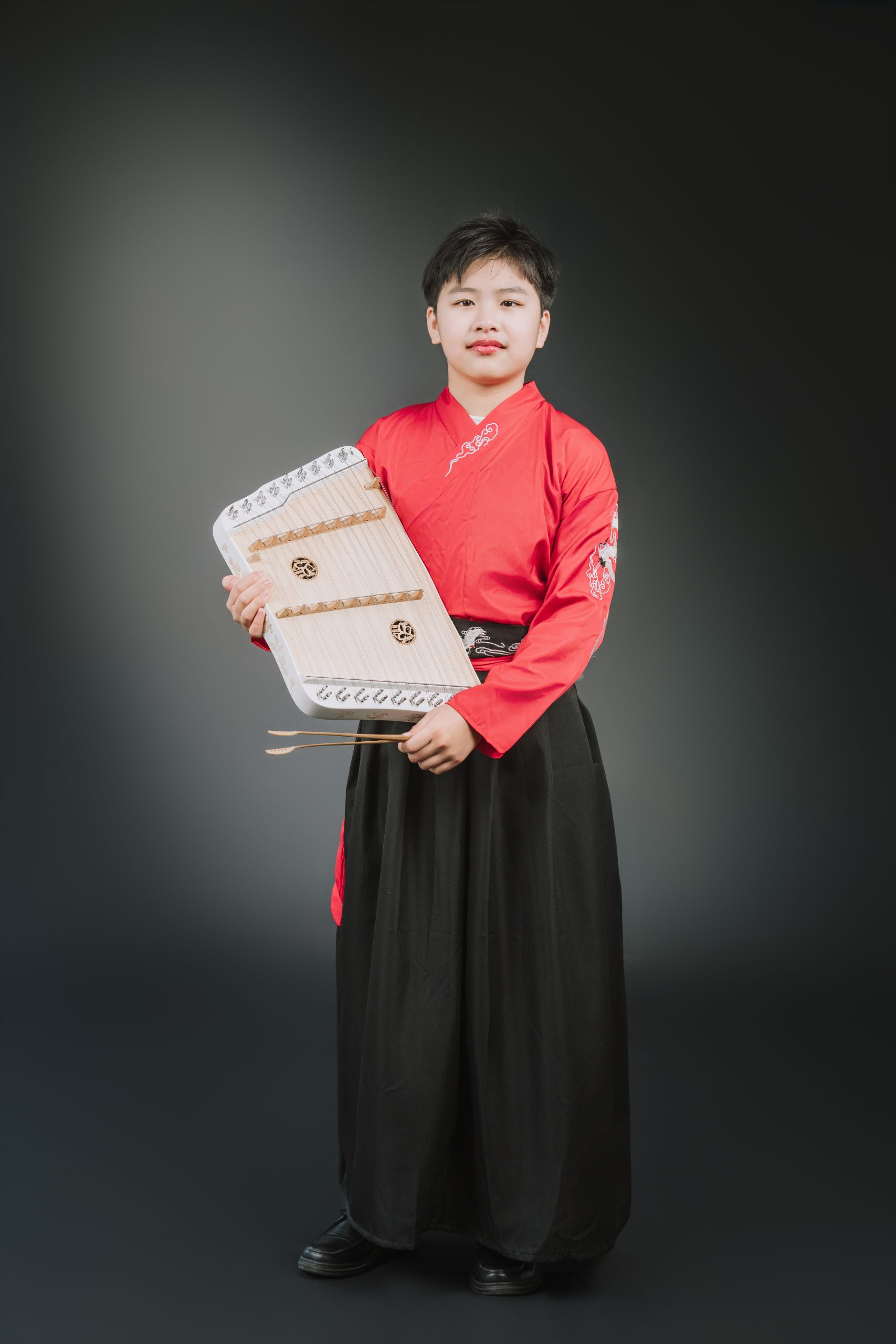 身穿紅黑漢服的男學生雙手端拿小揚琴與竹製琴槌棚拍