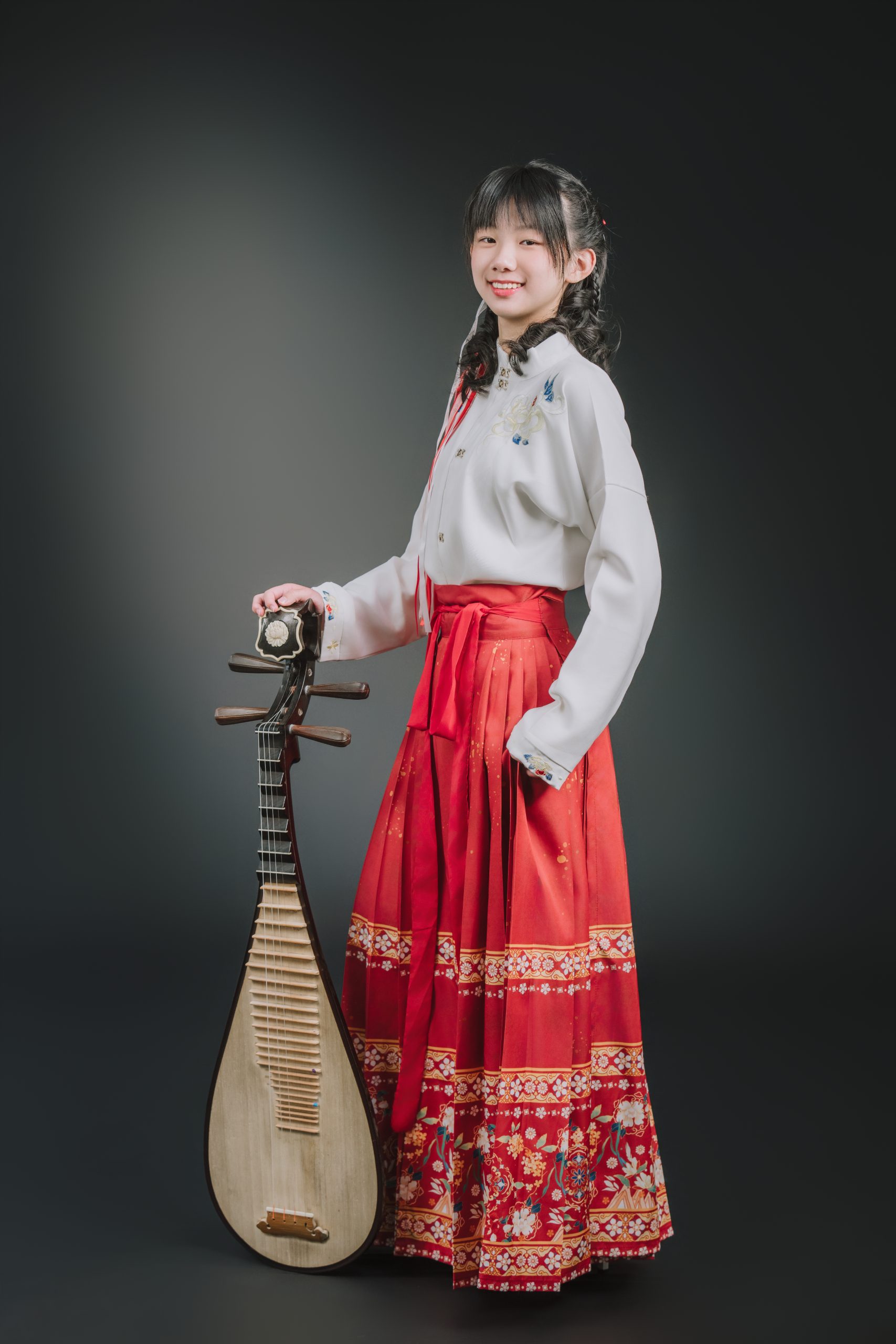 紅底金邊馬面裙女學生側身微笑手扶直立地面的琵琶
