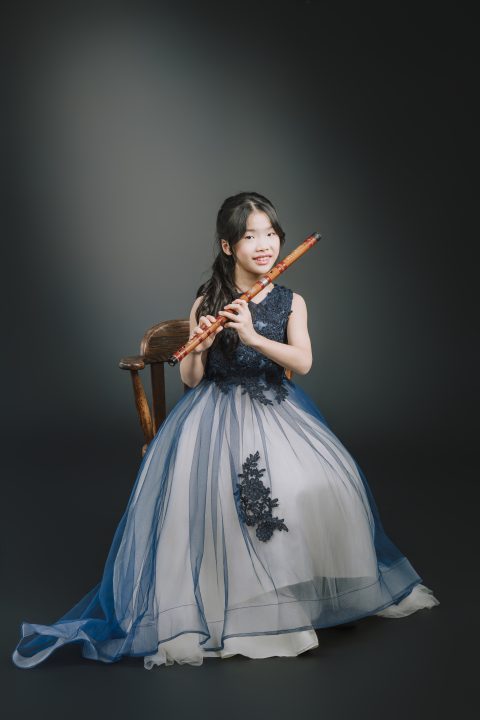 白色亮片薄紗洋裝女學生端坐木質扶手椅雙手持竹笛