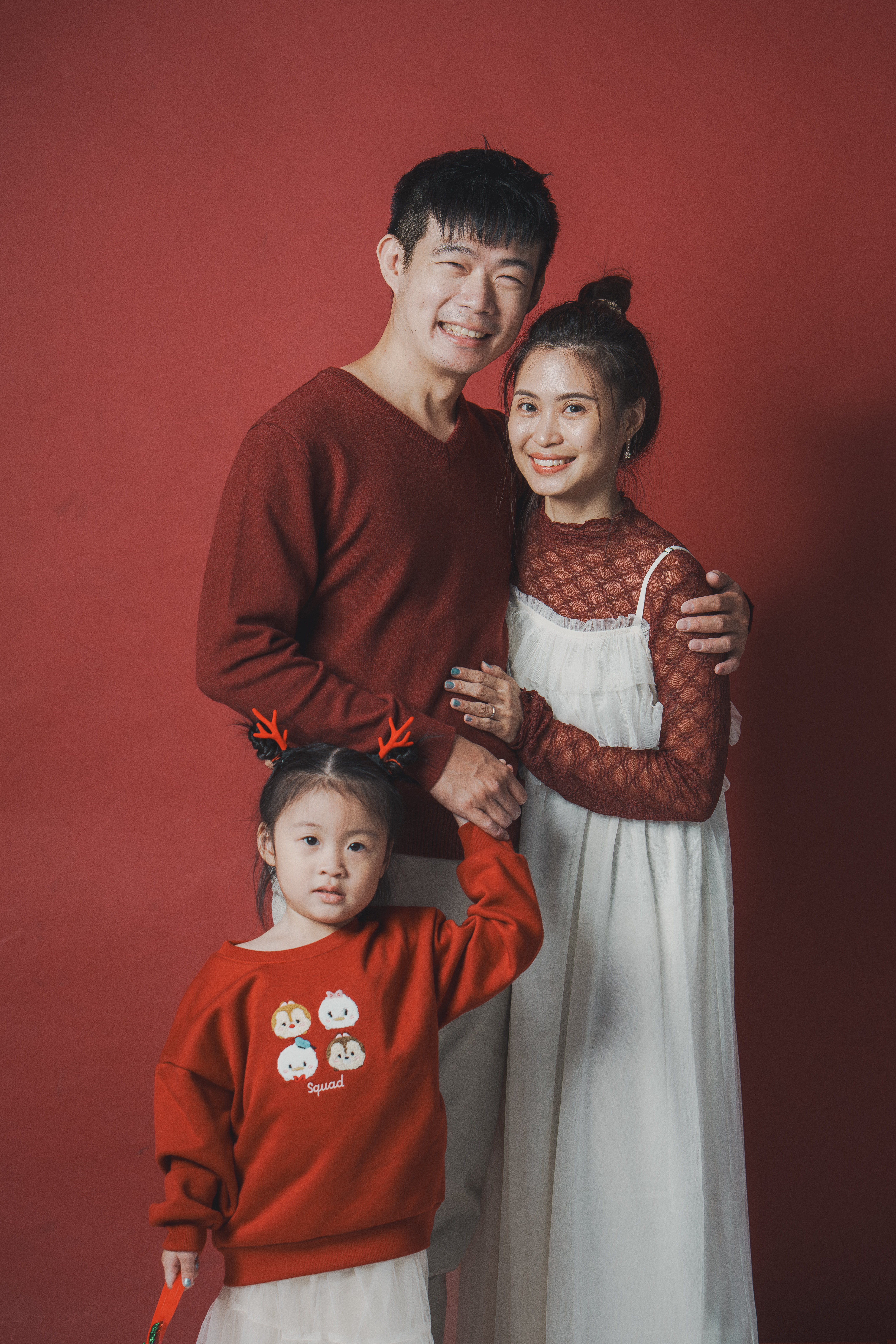 綁著小鹿角髮夾的女童站在前方，身後爸媽相擁微笑